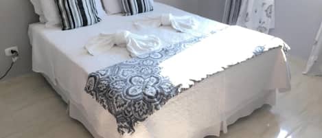 Una cama bien hecha con sábanas blancas y almohadas a rayas, una manta estampada y un enchufe en la pared.