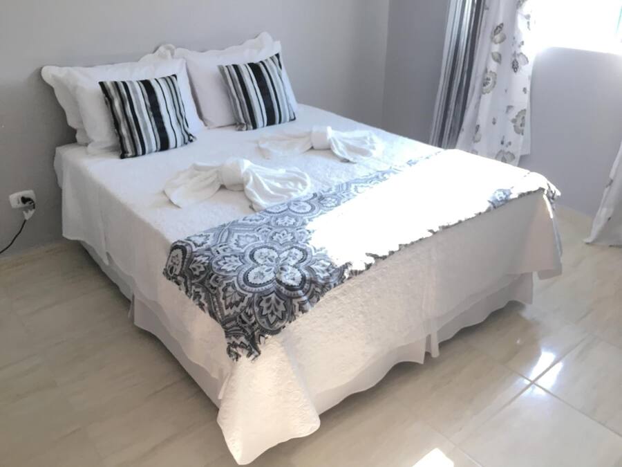 A neatly made bed with white linens and striped pillows, a patterned throw blanket, and a power outlet on the wall.