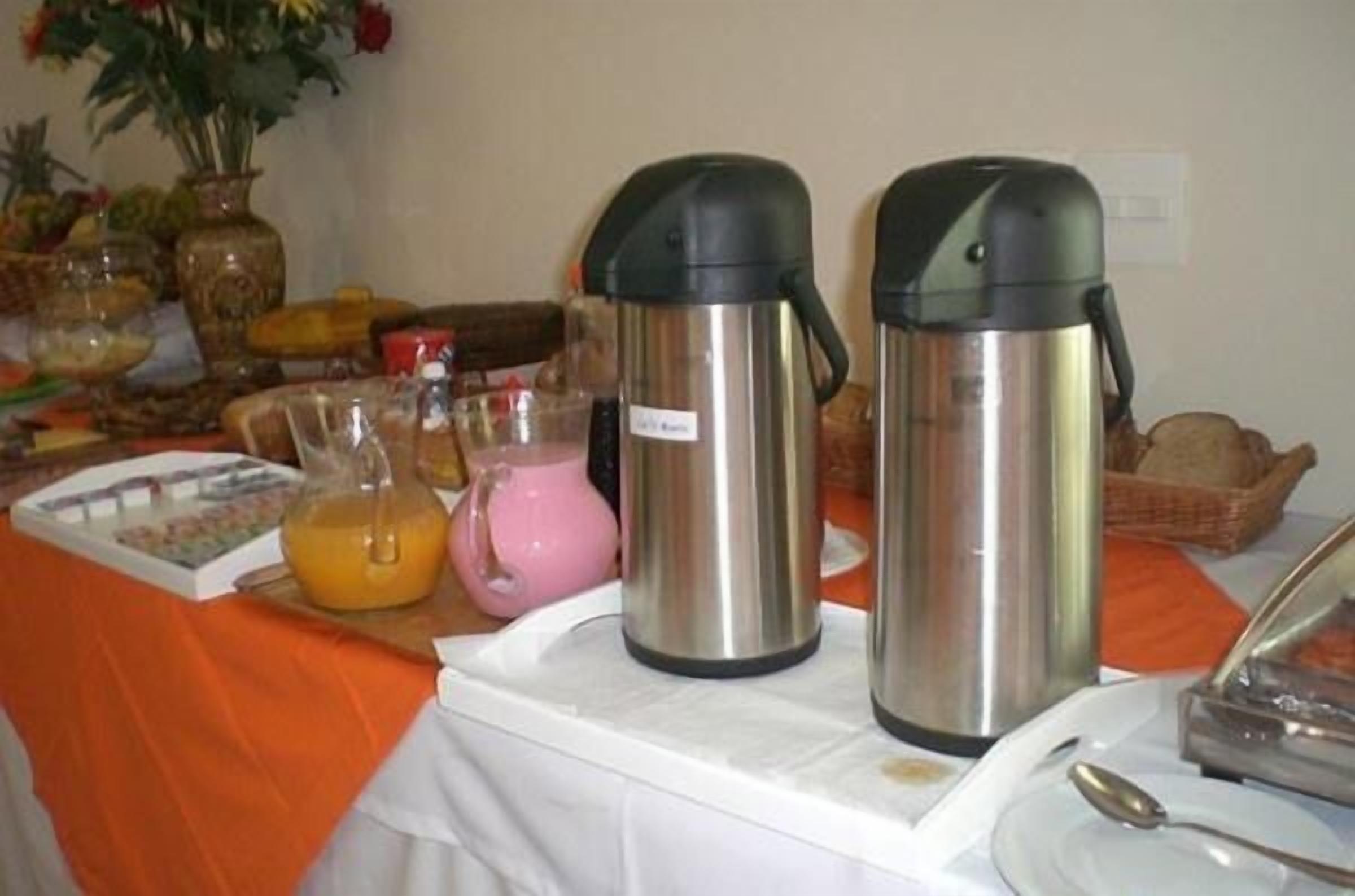A breakfast buffet setup with two stainless steel coffee makers, a pink pitcher, and a variety of food items on a table.