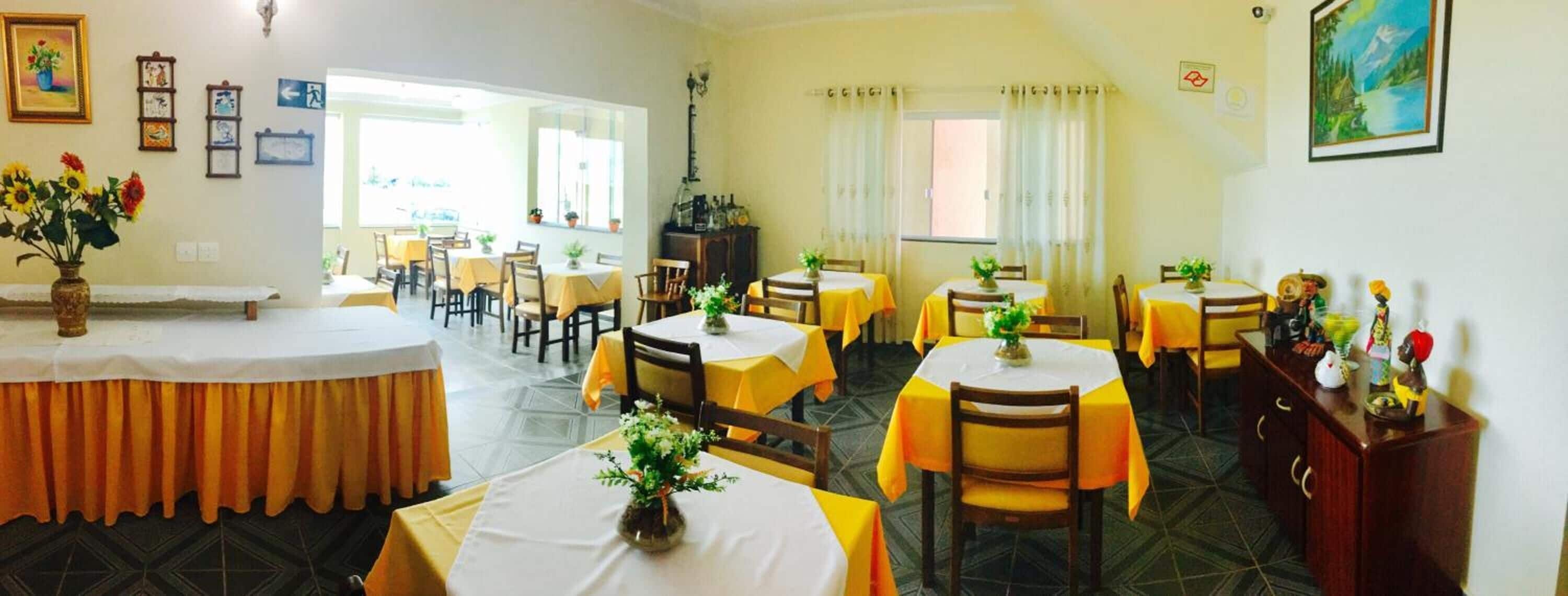 A dining area with round tables covered in yellow tablecloths, chairs, and potted plants.