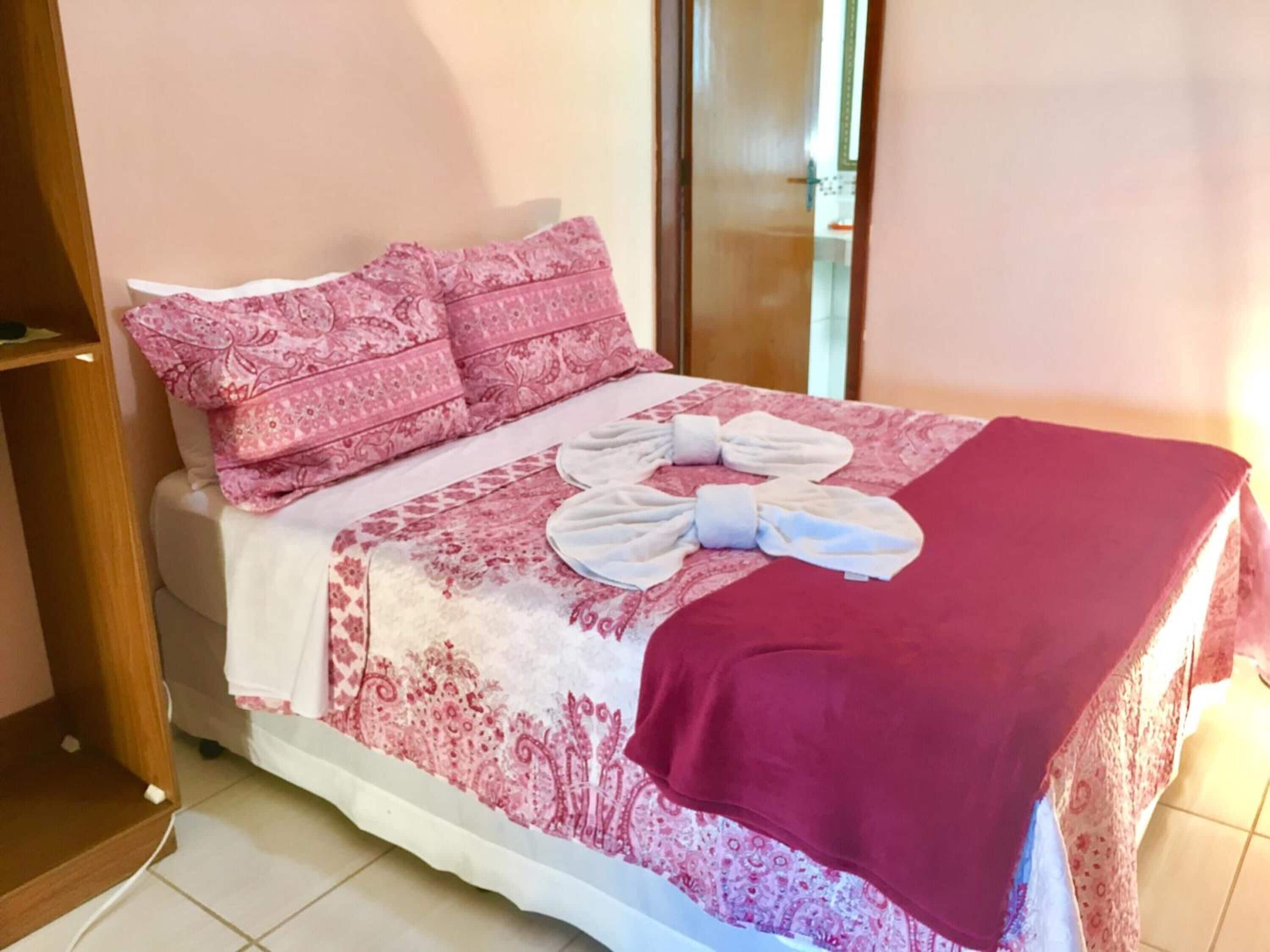 Ein ordentlich bezogenes Bett mit rosa gemusterten Bettwäsche und einer roten Decke.