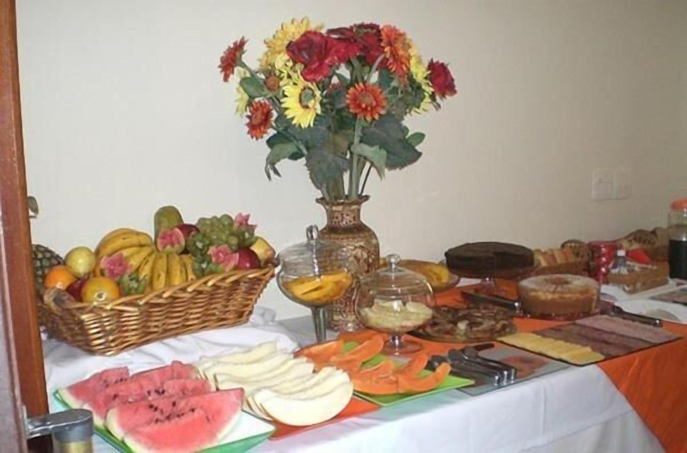 A buffet table with various food items, a vase of flowers, and a fruit basket.