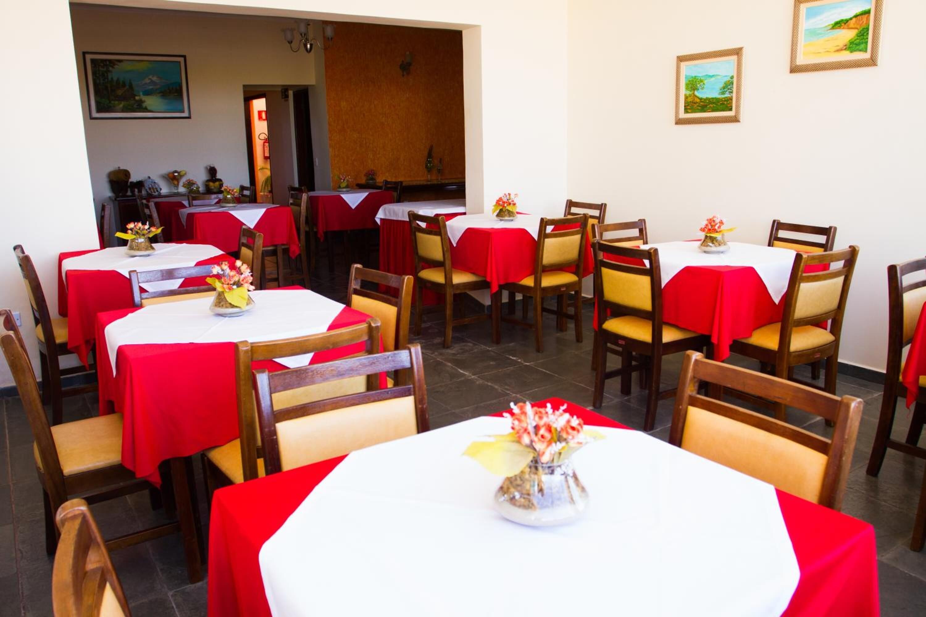 A restaurant with multiple tables covered in red tablecloths, wooden chairs, and flower centerpieces.