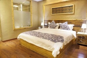 Una cama con estructura de madera, ropa de cama estampada, una mesita de noche con lámpara y una obra de arte colgada en la pared.