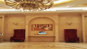 A grand lobby with a large chandelier, two red armchairs, a central painting, and a patterned floor. - Vienna Hotel (Dongguan)