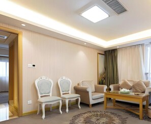 A hotel room with a seating area, two chairs, a sofa, a coffee table, and a large window with curtains.
