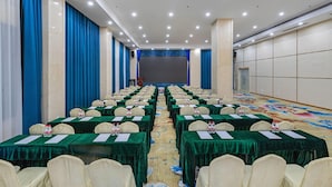 A conference room with rows of tables, chairs, and a stage at the front. - Vienna Hotel (Dongguan)
