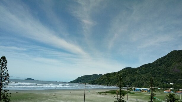 A beach with a clear sky, a sandy shore, and a hilly landscape in the background. - Praia Sul Studios (Peruíbe)