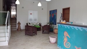 A spacious living area with a staircase, wicker furniture, and a colorful mural. - Praia Sul Studios (Peruíbe)