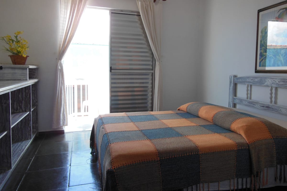 A bedroom with a bed, a nightstand, a potted plant, and a window with curtains.