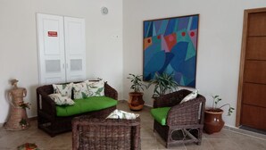 A room with wicker furniture, a green sofa, and a colorful abstract painting. - Praia Sul Studios (Peruíbe)