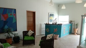 A spacious lobby with wicker furniture, a reception desk decorated with sea-themed elements, and a large abstract painting on the wall. - Praia Sul Studios (Peruíbe)