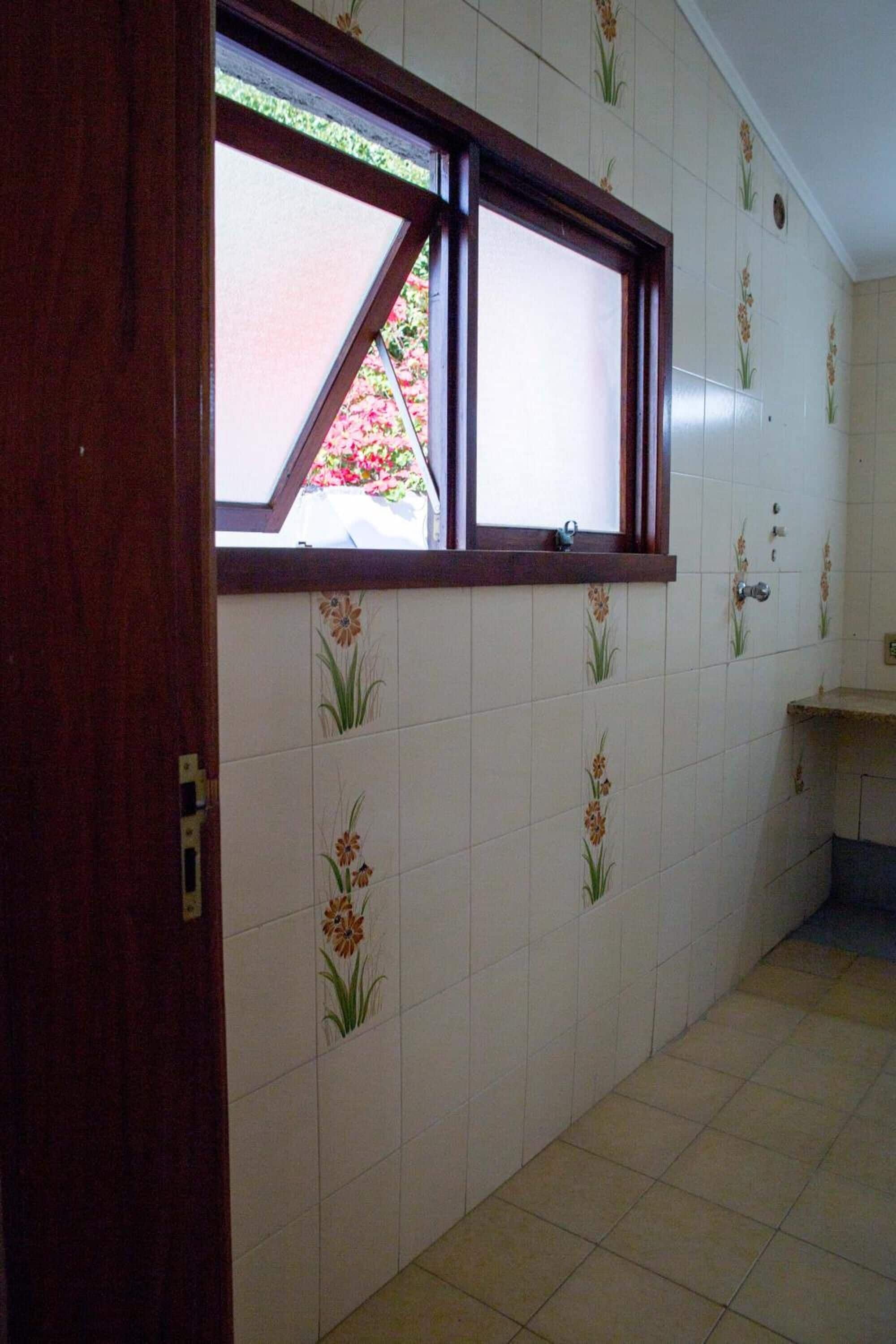 A bathroom with white tiled walls, a window with a wooden frame, and a small sink area.