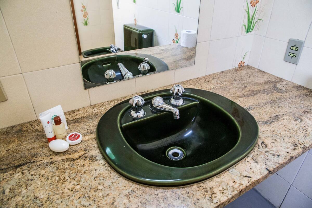 Een badkamer met een groene wastafel, twee kraanwerkstukken en een spiegel.