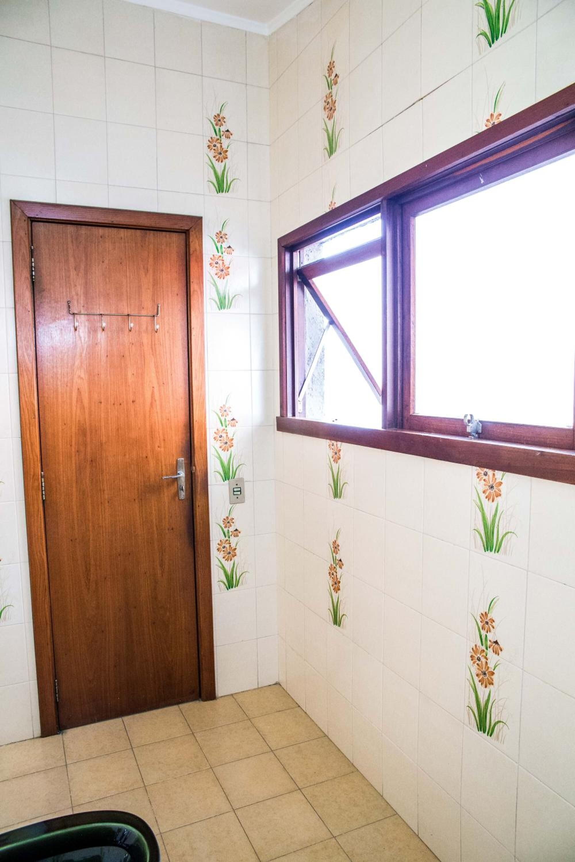 A room with a wooden door, a window with a wooden frame, and tiled walls with floral patterns.