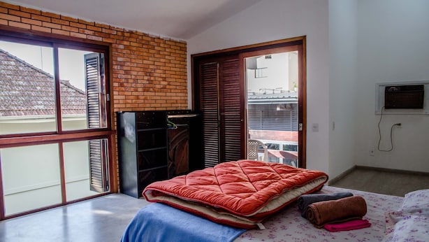 Een slaapkamer met een groot bed, een blauwe deken, een rode sprei en een bloemenbeddelspray. Er is een bakstenen muur en een schuifdeur die leidt naar een balkon.