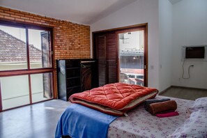 Un dormitorio con una cama grande, una colcha azul, una colcha acolchada roja y un edredón estampado. Hay una pared de ladrillo y una puerta corredera que da a un balcón.