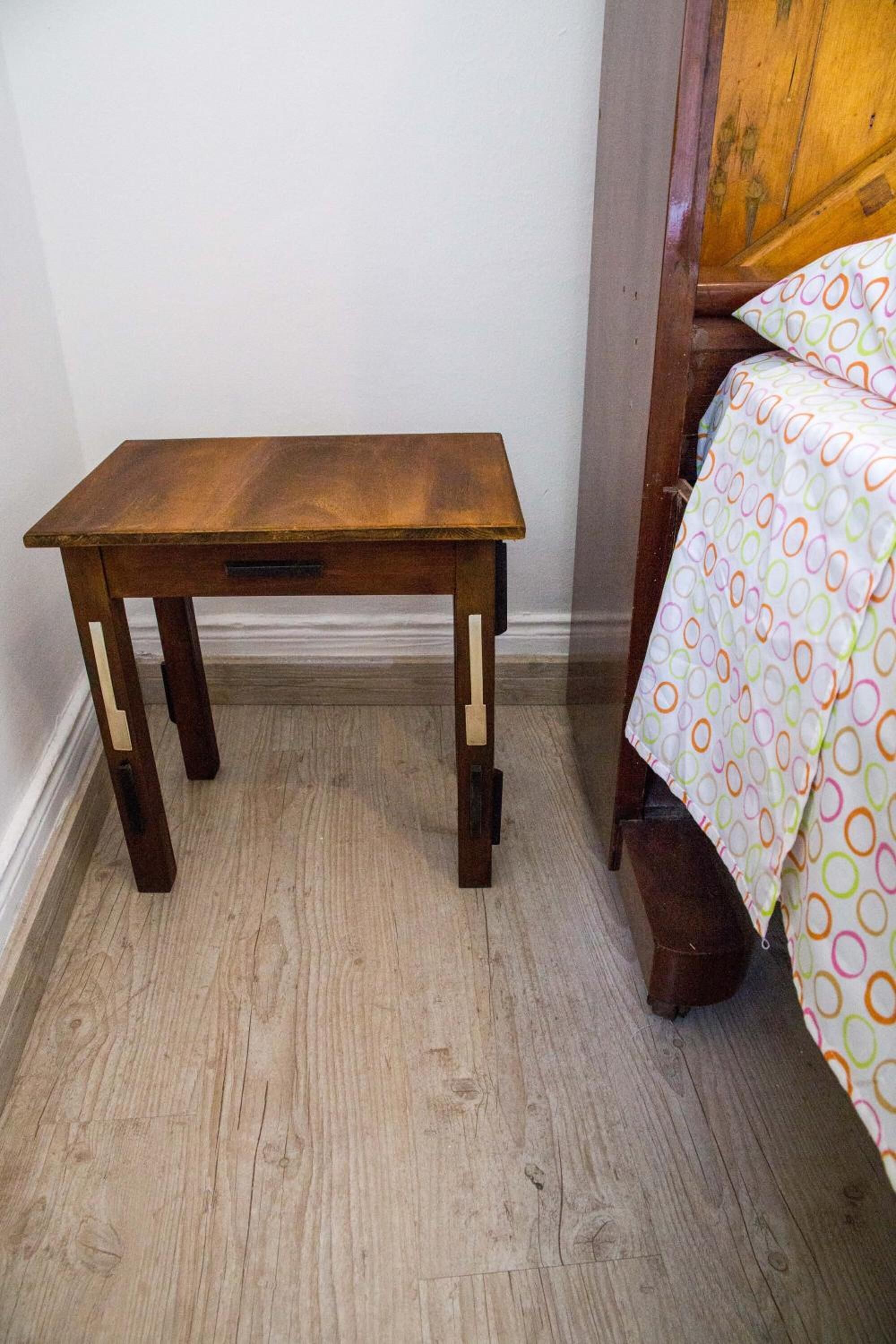 Un comodino in legno con cassetti, posizionato accanto a un letto con una coperta a fantasia colorata.