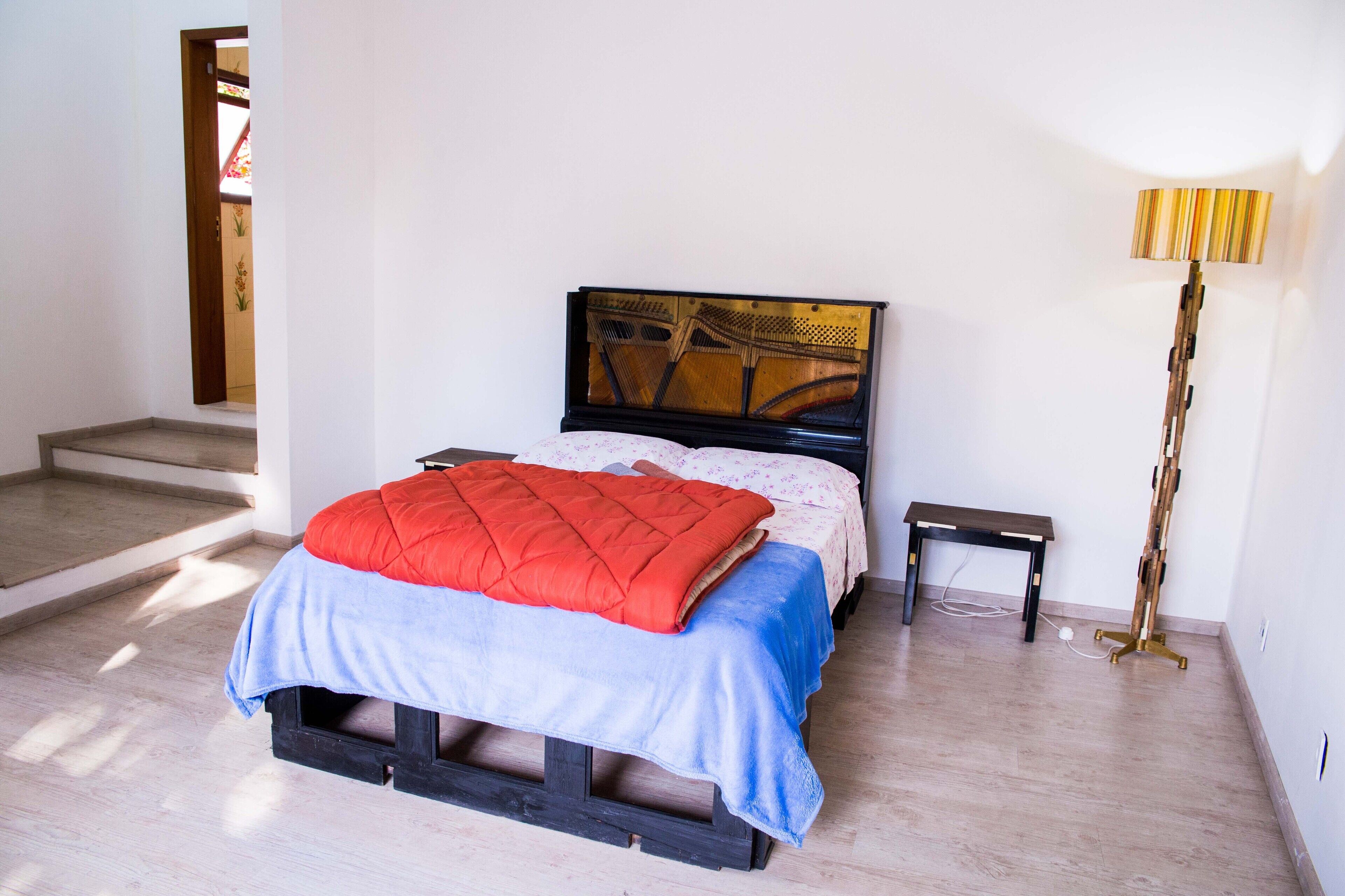 A bedroom with a bed, a bedside table, a lamp, and a wooden floor.