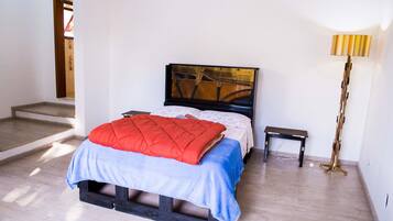 A bedroom with a bed, a bedside table, a lamp, and a wooden floor.