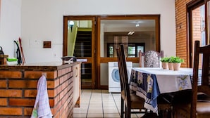 Een keuken met een met baksteen belegd aanrecht, een eettafel met stoelen, en een uitzicht op de woonkamer door een open deur.