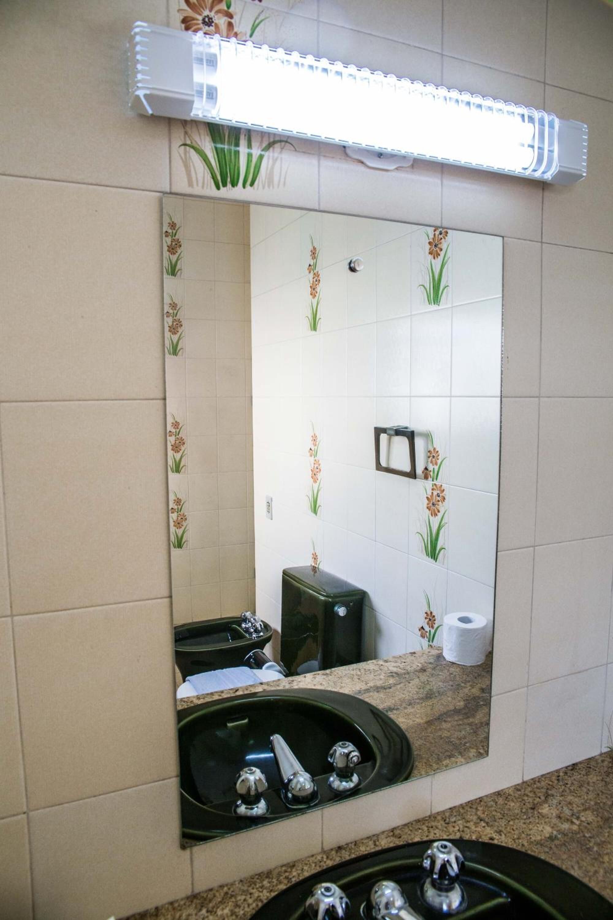 A bathroom with a large mirror, a sink, a towel rack, and a toilet paper holder.