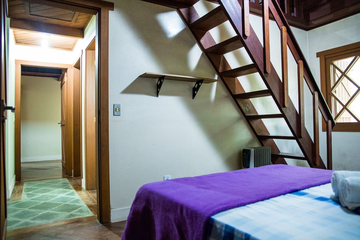 A room with a bed, a wooden staircase, and a hallway leading to another room.
