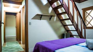A room with a bed, a wooden staircase, and a hallway leading to another room.