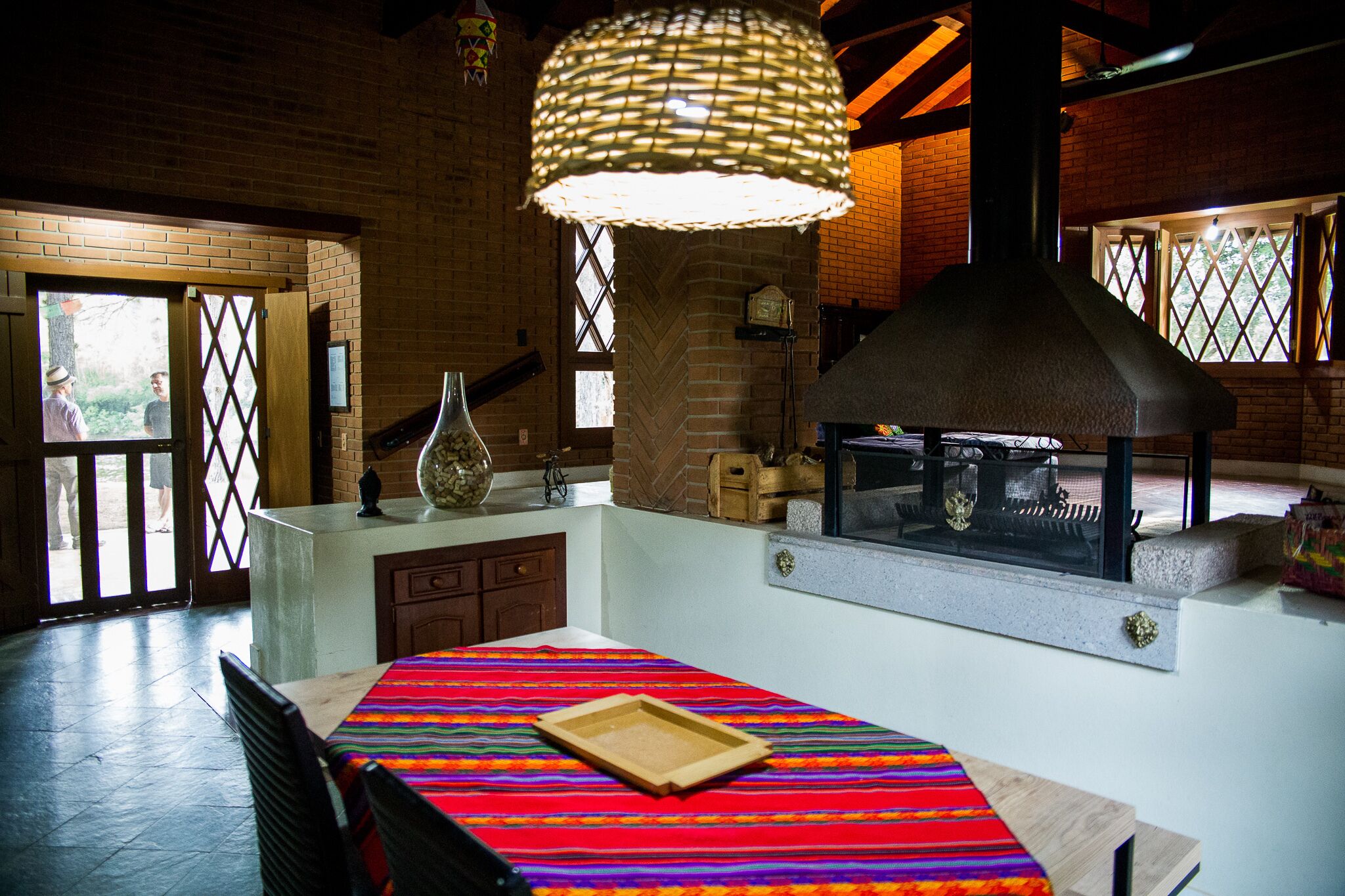 A rustic kitchen with a brick wall, a large woven light fixture, and a wood-burning stove.