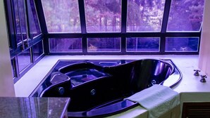 A corner bathroom with a freestanding bathtub, large windows, and a view of a forest. - OM B&B & Spa (Viamao)