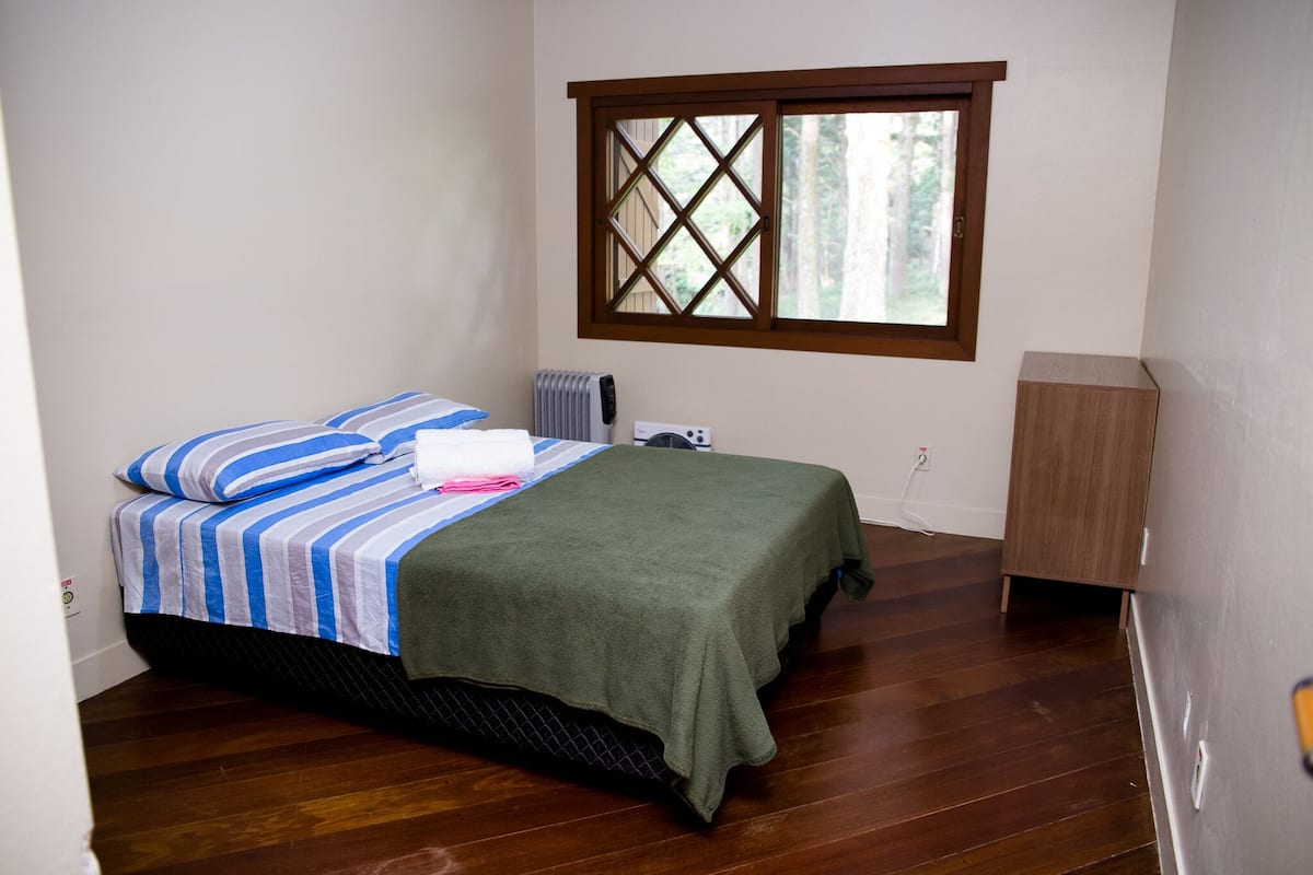 A bedroom with a bed, a window, a radiator, and a wooden cabinet.