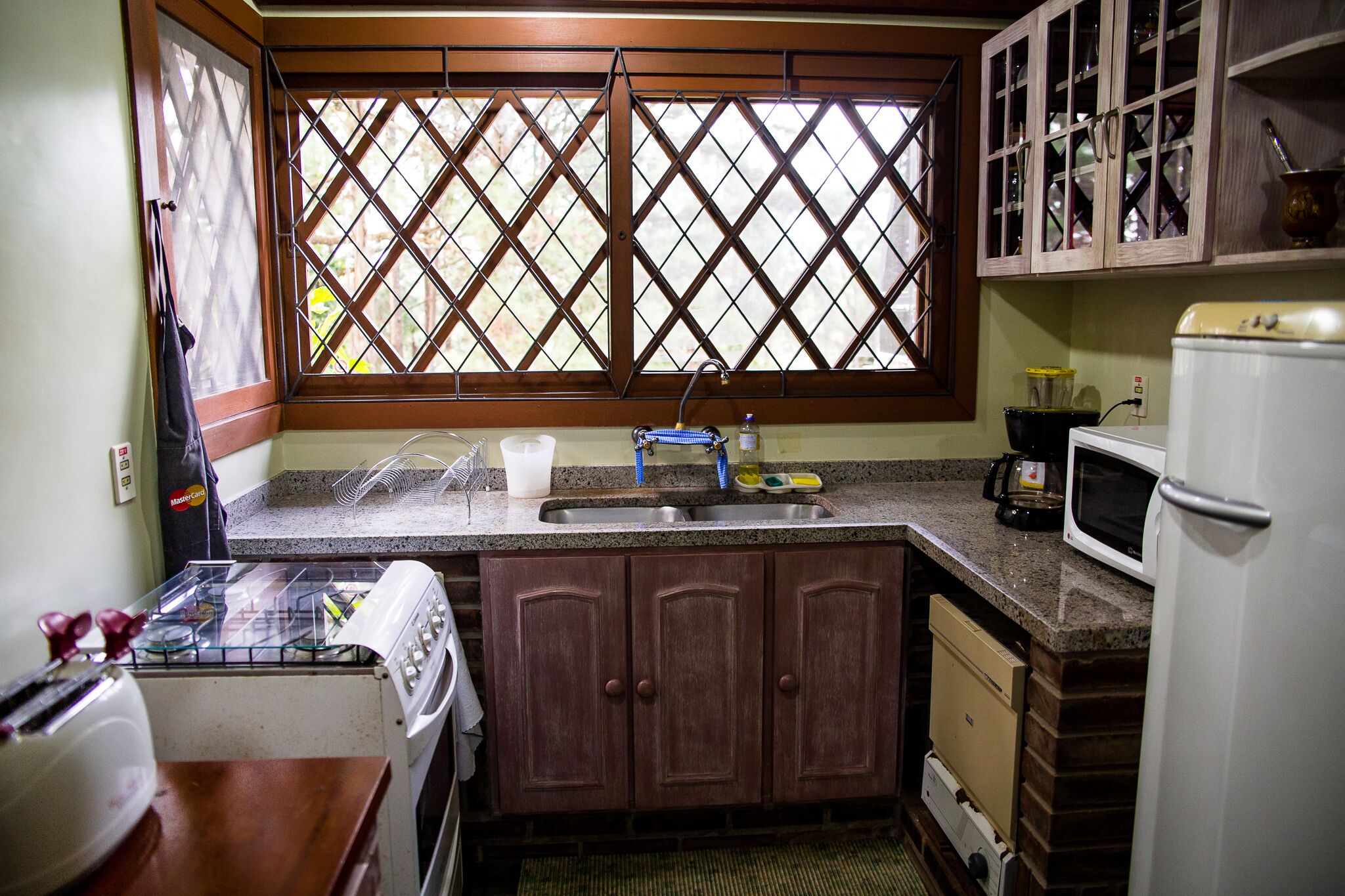 A compact kitchen with a window, sink, stove, cabinets, and a microwave.