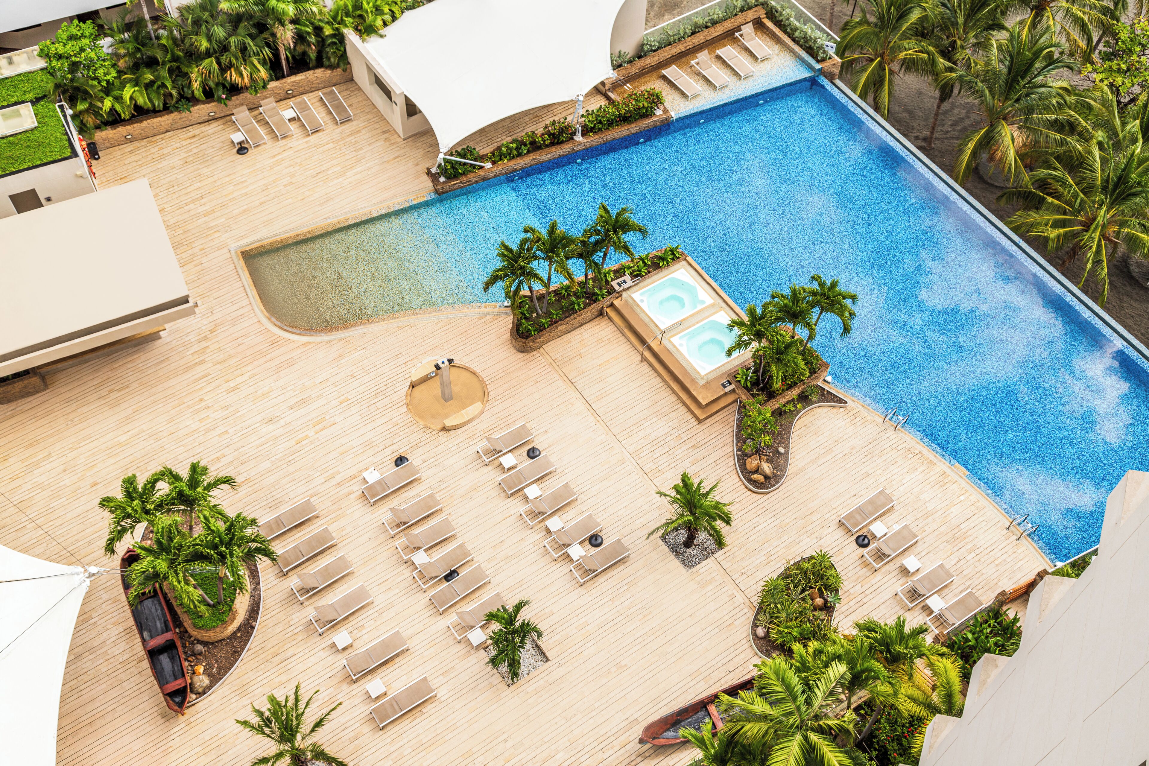 Uma área de piscina no terraço com espreguiçadeiras, palmeiras e uma pequena banheira de hidromassagem.
