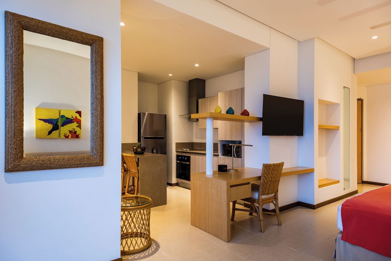 Una habitación de hotel moderna con zona de comedor, kitchenette y televisor montado en la pared.