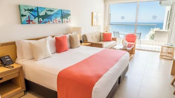 A hotel room with a large bed, a sofa, a small table, and a view of the sea.