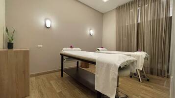 A modern spa room with two massage tables, a wooden cabinet, and a potted plant.