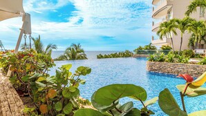 A poolside view with a clear view of the ocean, surrounded by lush greenery and a modern building. - Hotel Irotama Reservado (Santa Marta)