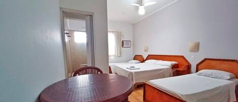 A hotel room with two beds, a dining table, and a ceiling fan.