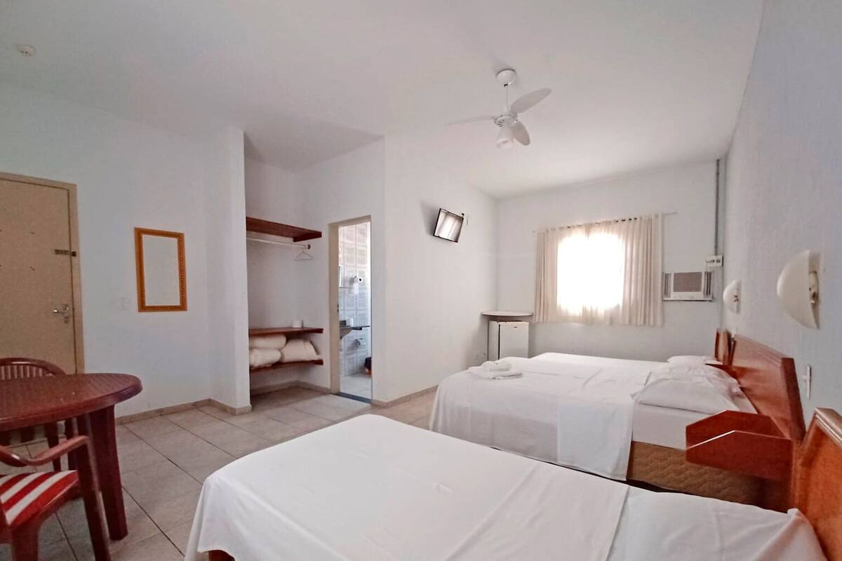 Habitació d'hotel amb dos llits, una taula de treball, una cadira, un armari, un ventilador de sostre i una televisió.