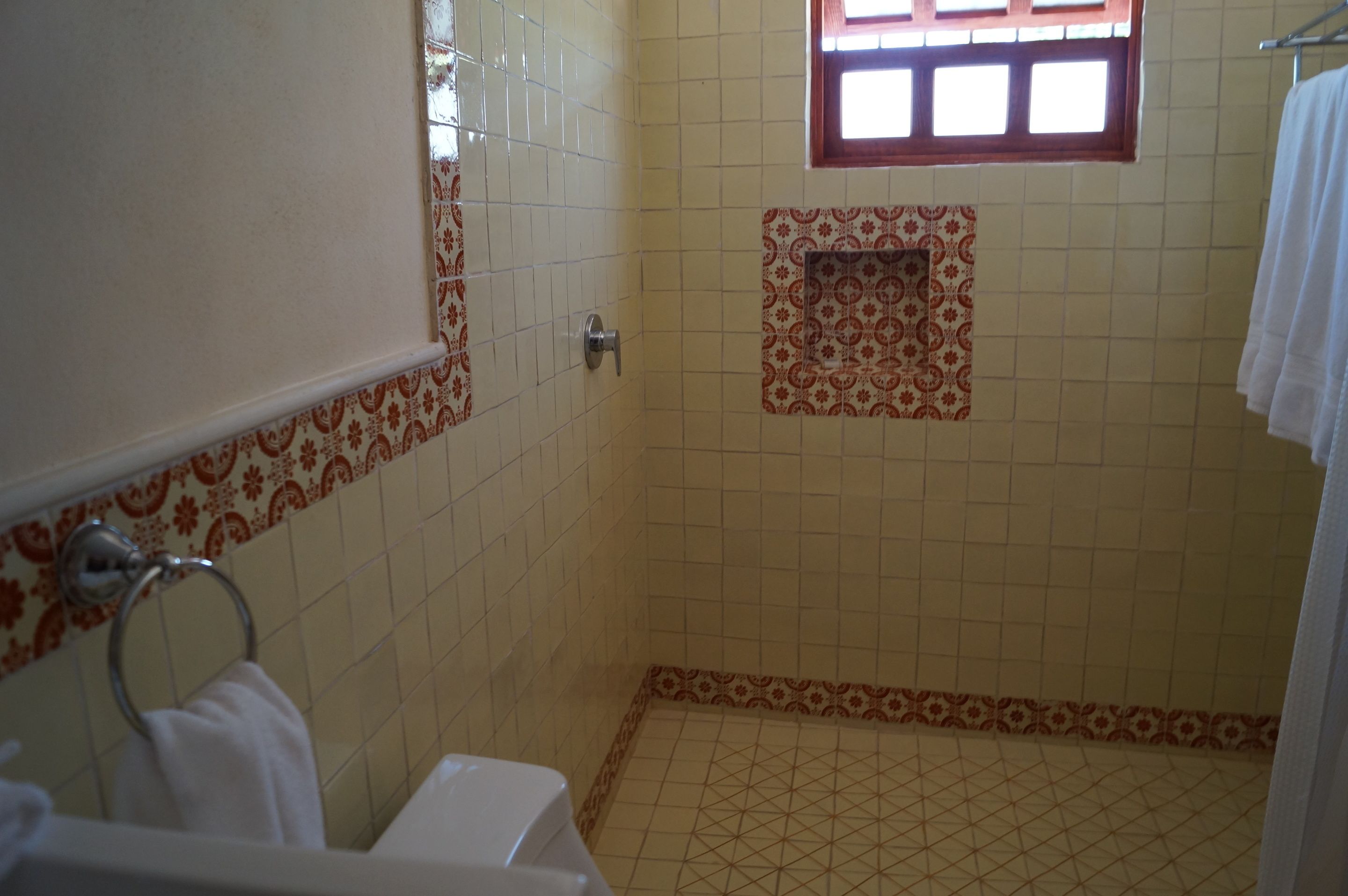 A bathroom with a tiled floor, a toilet, a sink, a towel rack, and a window.