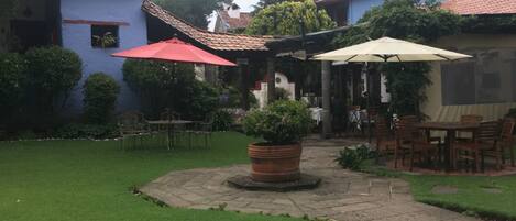 Un patio con césped, una mesa de madera con sillas y una planta en maceta.