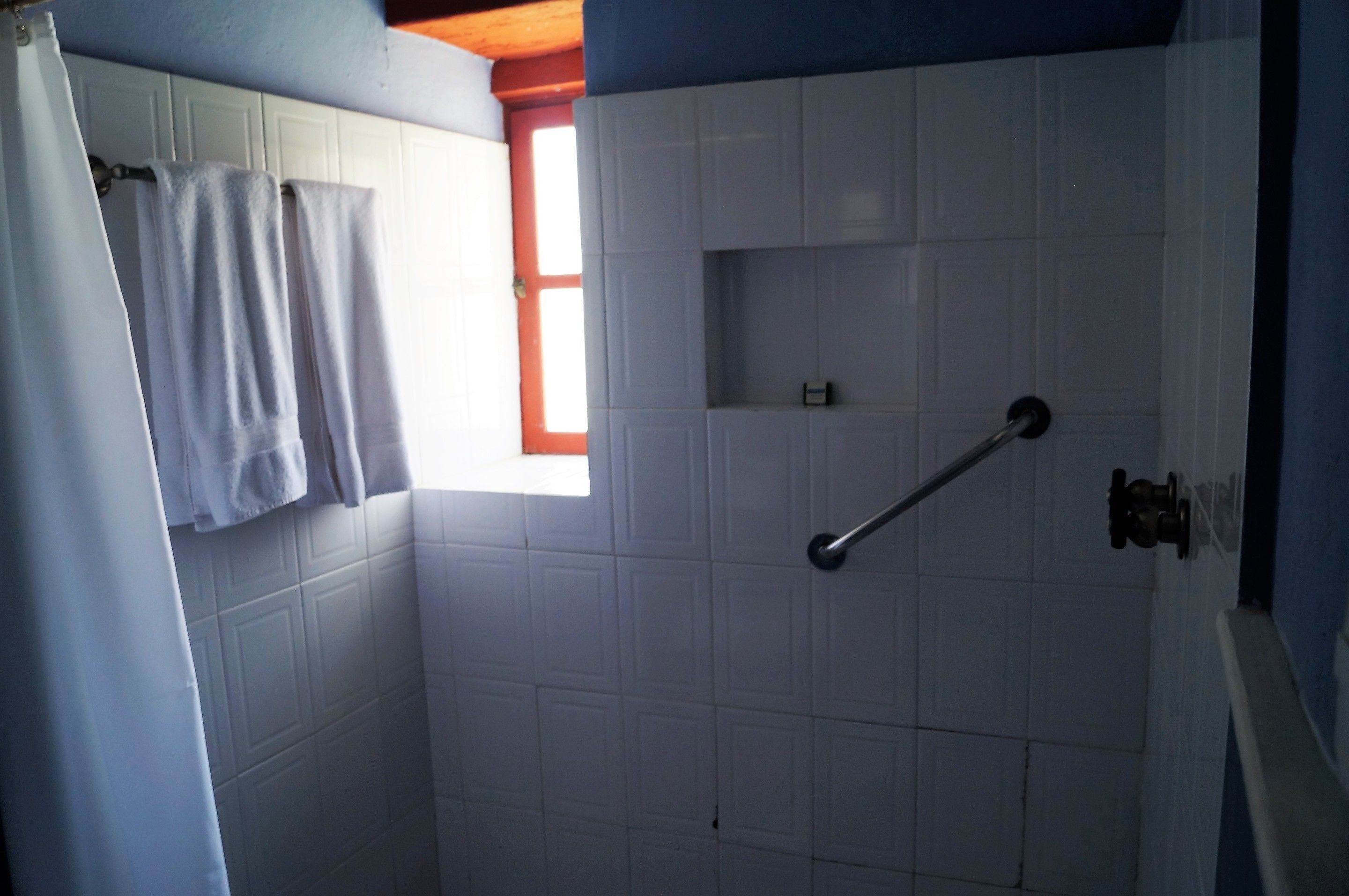 A bathroom with white tiled walls, a window, and a shower with a grab bar.