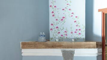 Una chimenea con repisa blanca, un estante pequeño con botellas de agua y un mural floral decorativo.