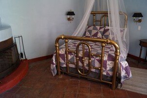 Una cama con estructura metálica y dosel, colcha estampada y dos lámparas fijadas a la pared.