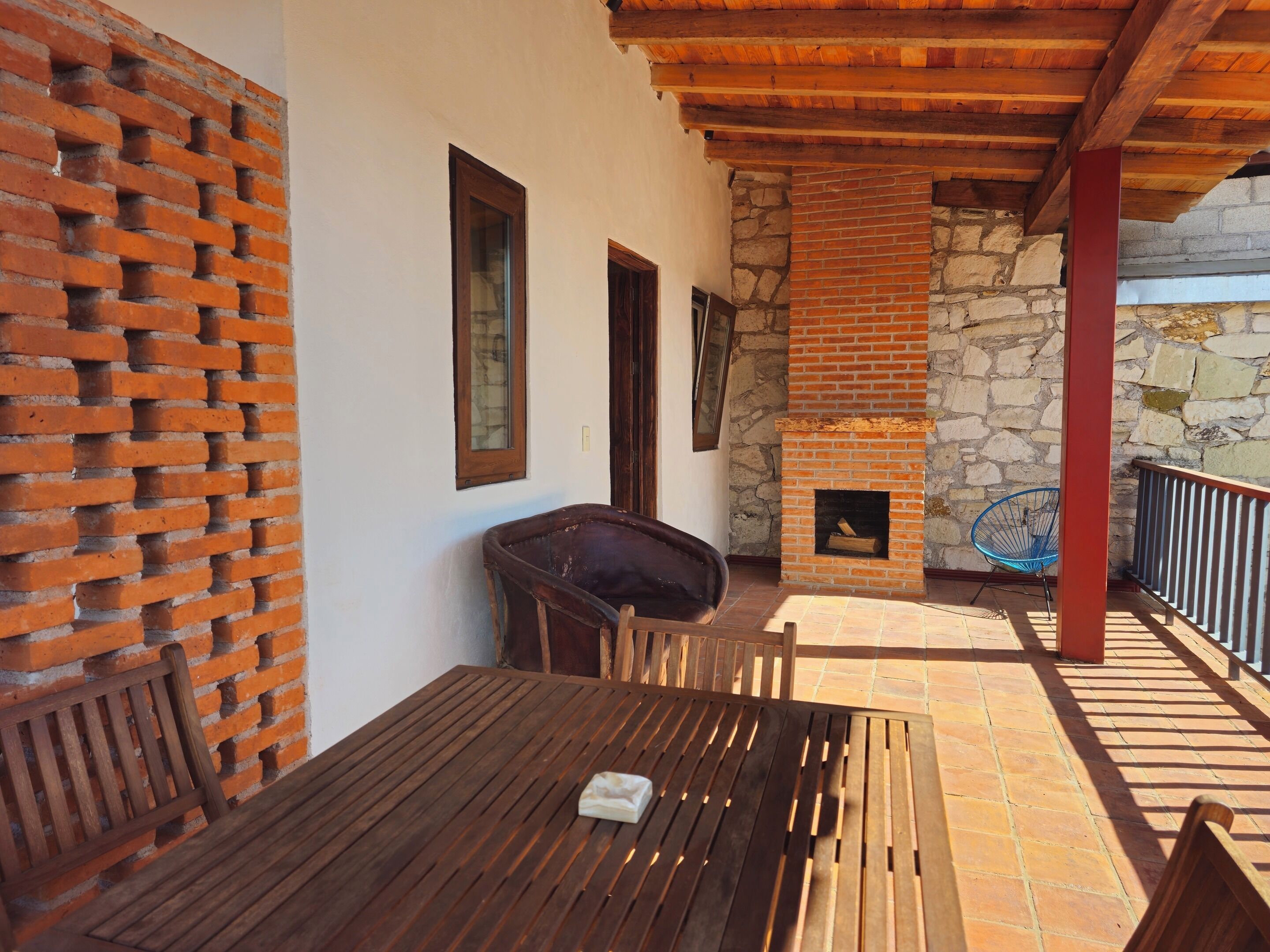 A wooden table and chairs on a patio with a stone wall and a brick fireplace.