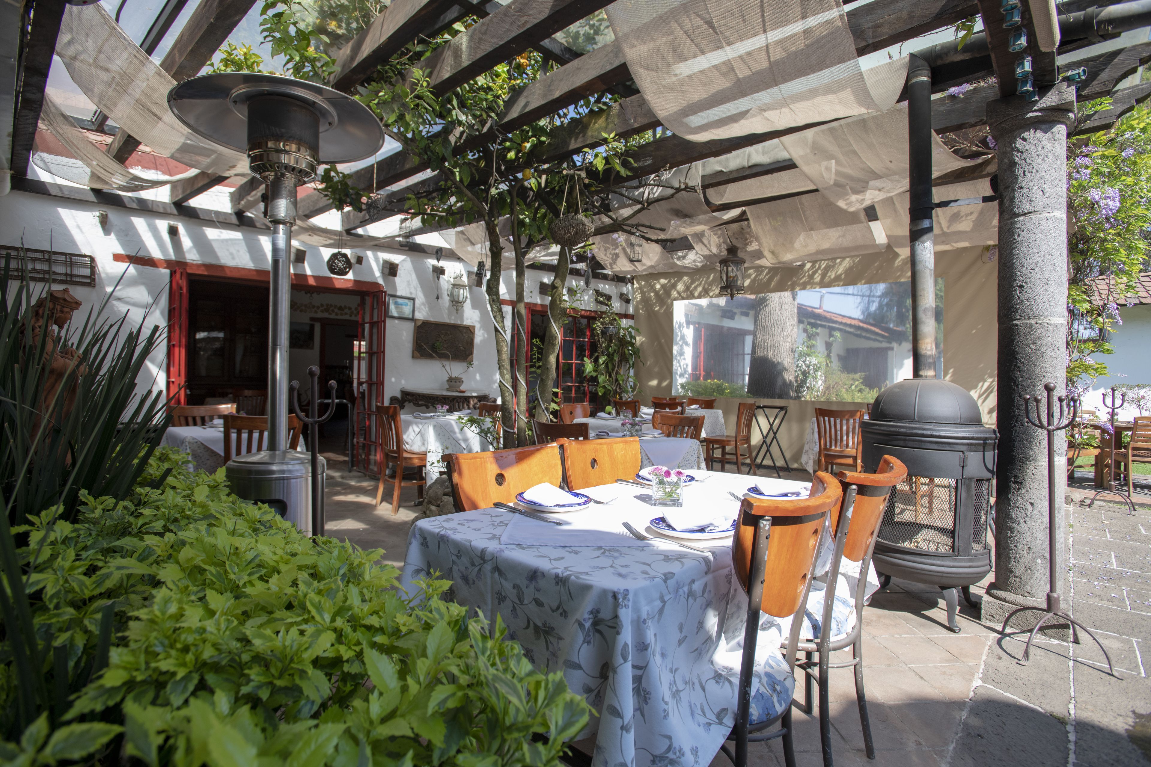 Un área de comedor al aire libre con mesas y sillas, un techo decorativo y una chimenea de piedra.