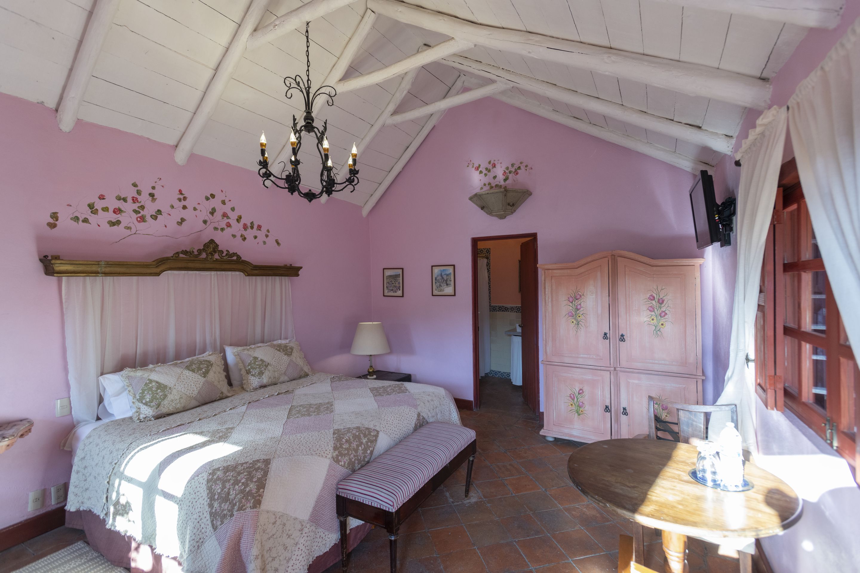 A bedroom with a bed, bench, dresser, and a table with a lamp.