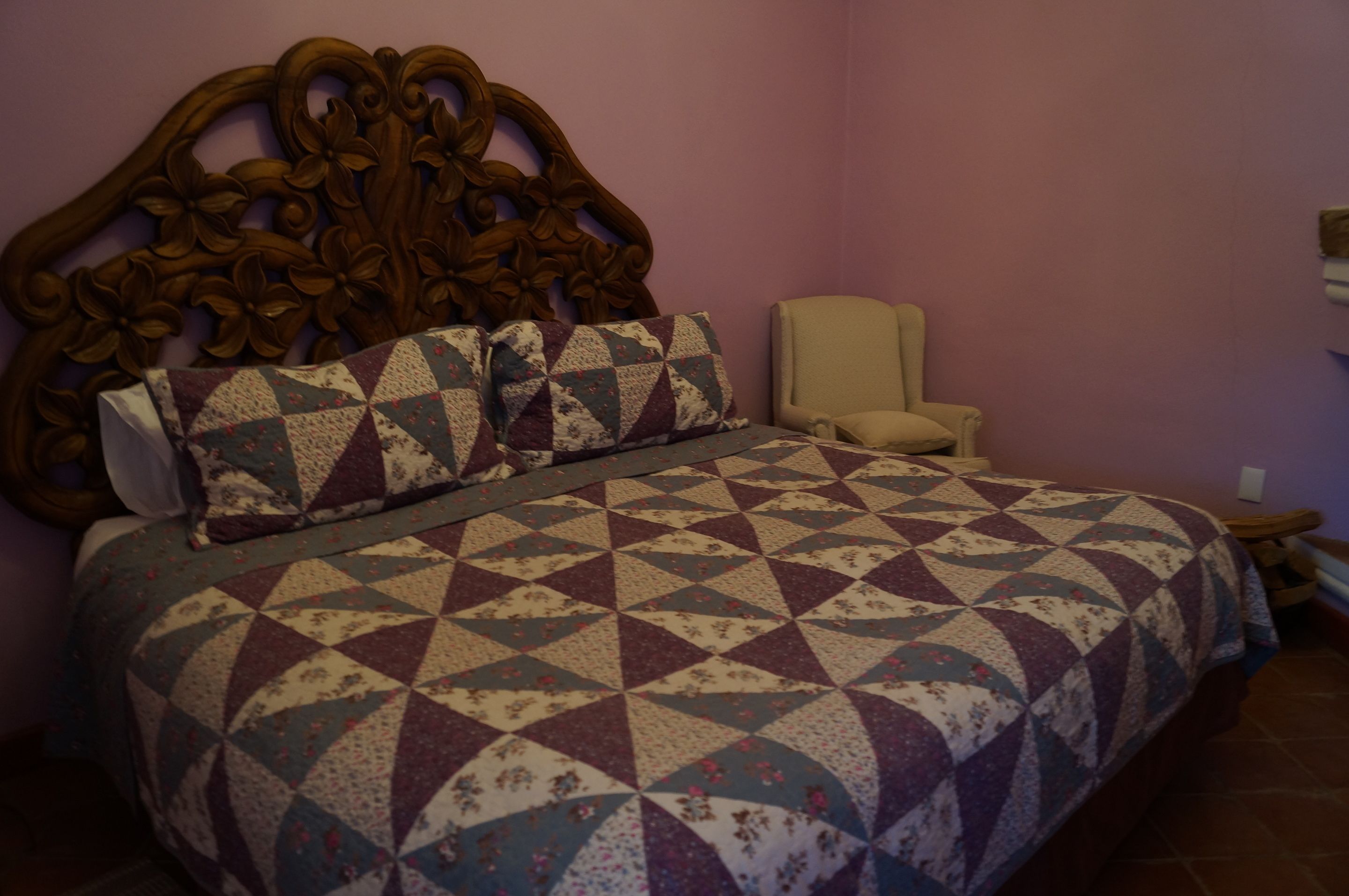 A bedroom with a wooden headboard, a floral-patterned bedspread, and a plain chair.