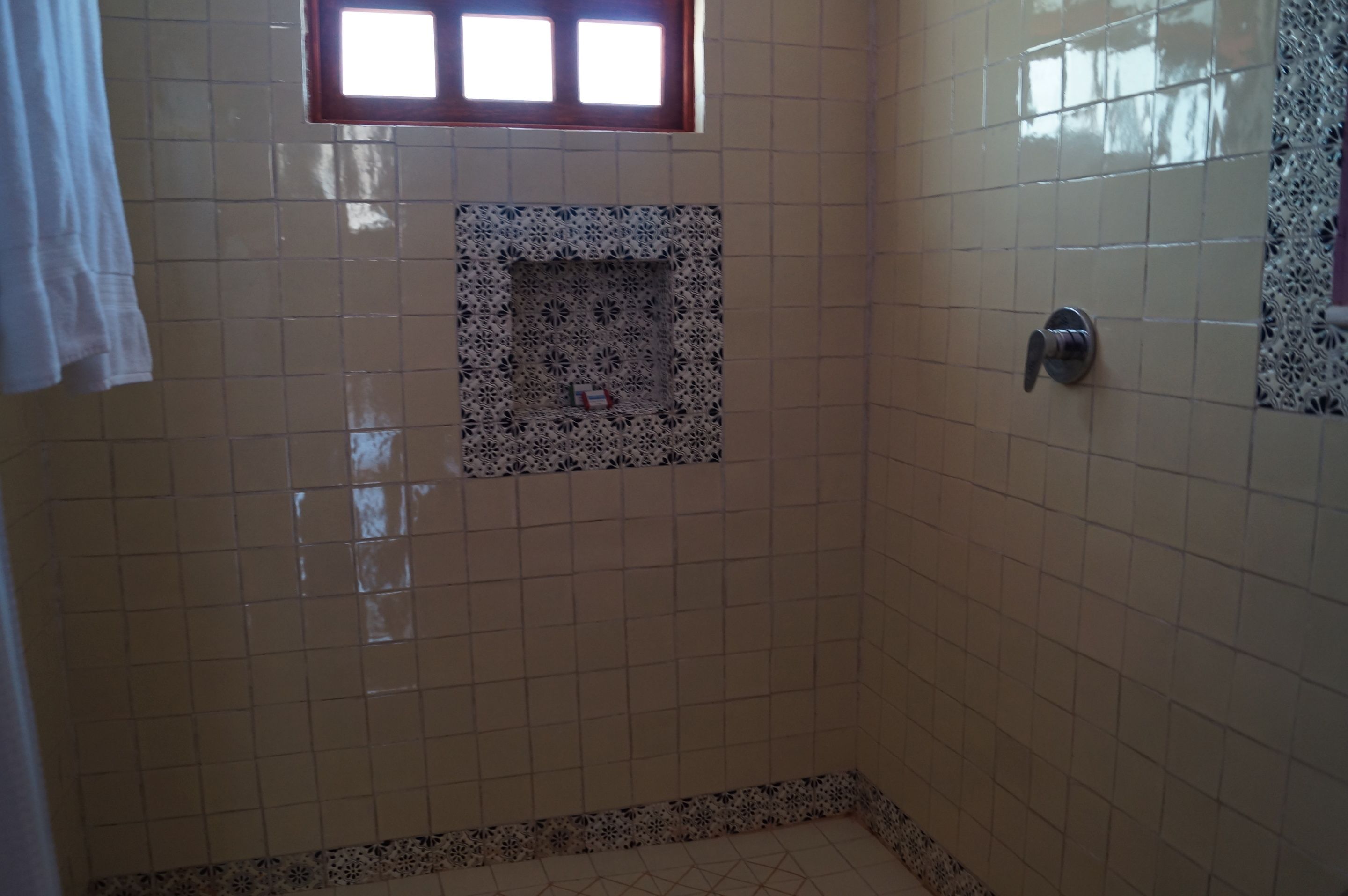 A bathroom with beige tiled walls, a patterned tile feature, a window, and a shower area.