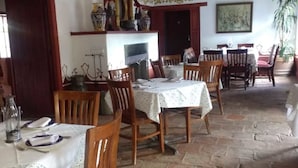 A dining area with stone flooring, wooden chairs, and tables set with white tablecloths.